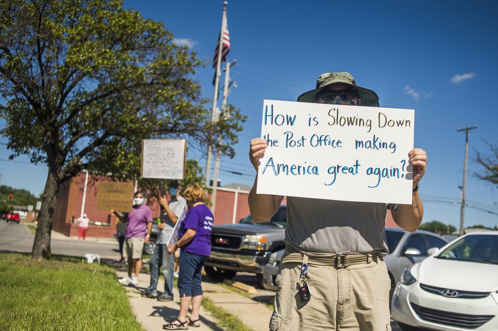 Eric Severson holds a sign as a few dozen people gather in front of the United States Post Office on Rodd St. to protest recent changes to the U.S. Postal Service under new Postmaster General Louis DeJoy Tuesday, Aug. 11, 2020 in Midland, Mich.